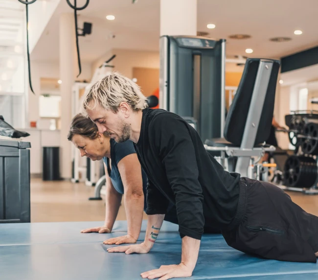 Personal Trainer zeigt Übung auf der Matte gemeinsam mit der Kundin vor
