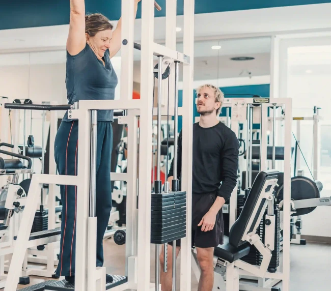 Personal Trainer beobachtet Übung von der Kundin in der Klimmzugmaschine