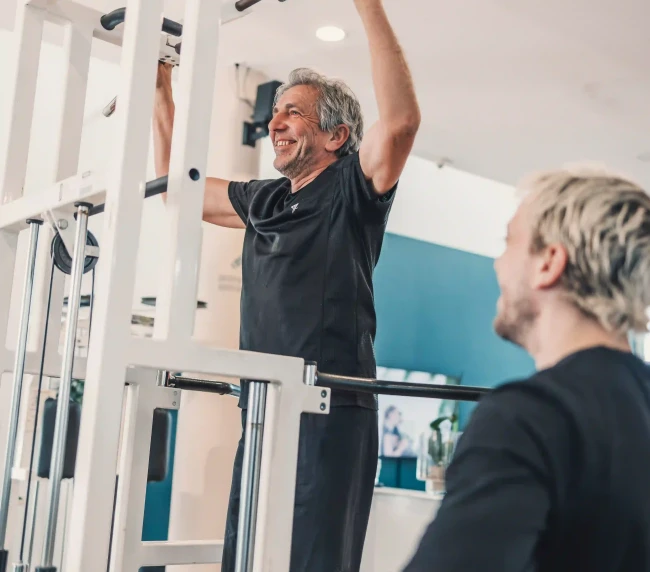 Personal Trainer beobachtet Übung von dem Kunden in der Klimmzugmaschine